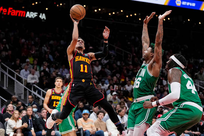 Trae Young jumps shooting the ball as two Celtics defenders stand in front of him